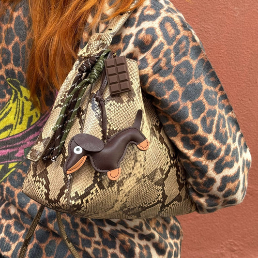 Person wearing a leopard print jacket with a small backpack featuring a dachshund charm.