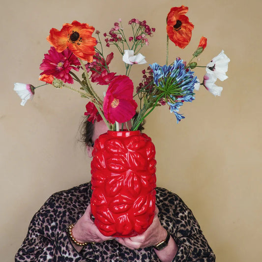 Person holding a red textured vase with colorful flowers against a beige background