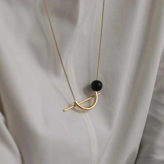A gold-colored necklace with a black spherical pendant, displayed on a light shirt.