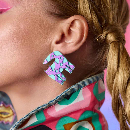 Close-up of a person wearing colorful earrings with a pink and blue background