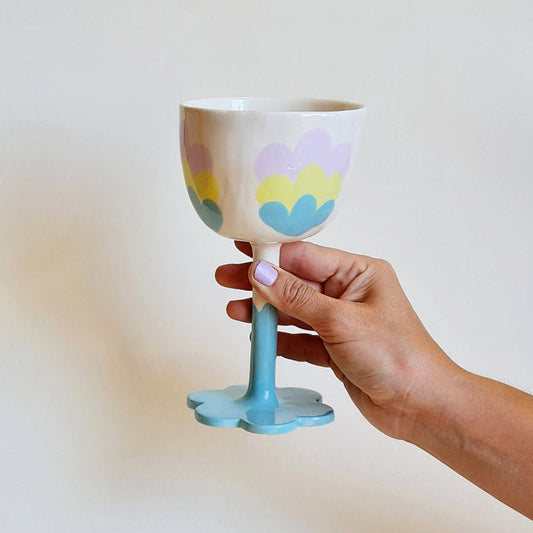 Hand holding a decorative ceramic cup with pastel floral design on a plain background
