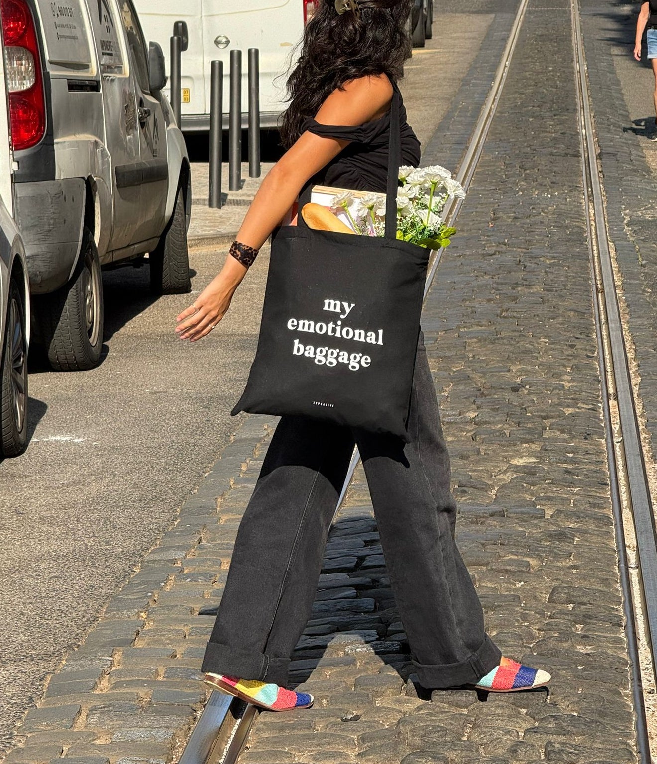 Person walking on a street holding a black bag labeled 'my emotional baggage'.