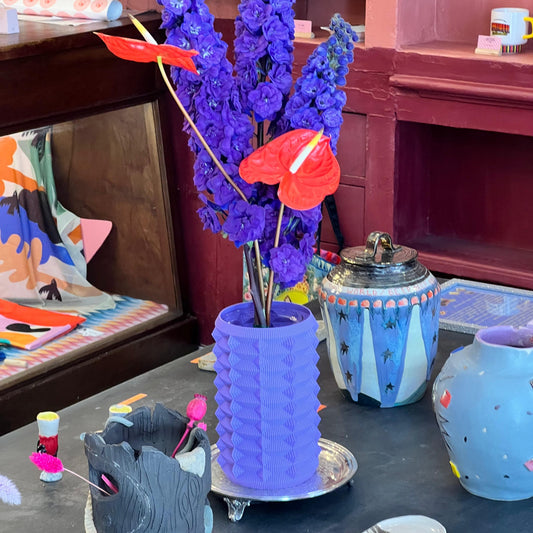 Decorative setup with purple vase, colorful flowers, and small figurines on a table.