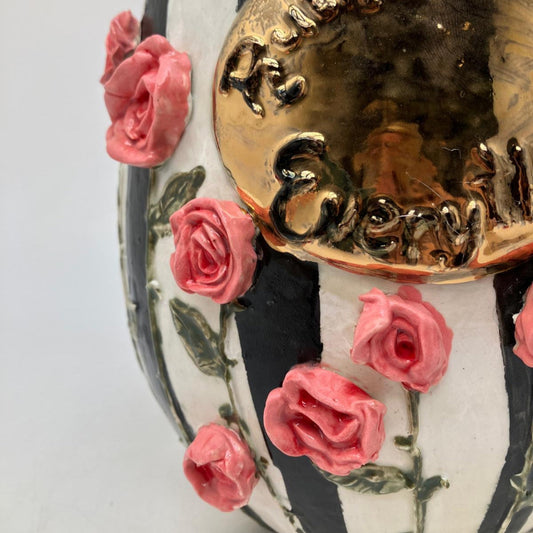 Decorative item with gold text, pink roses, and black and white striped pattern on a light gray background