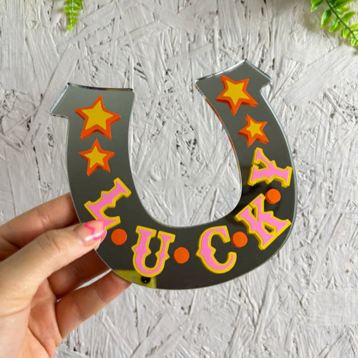 Horseshoe-shaped sign with 'LUCKY' text and stars held by a hand against a textured white background.