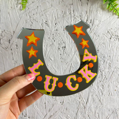 Horseshoe-shaped sign with 'LUCKY' text and stars held by a hand against a textured white background.