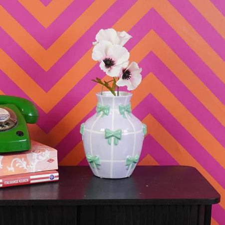 Black cabinet with a green phone and white vase against a pink and orange chevron wall.