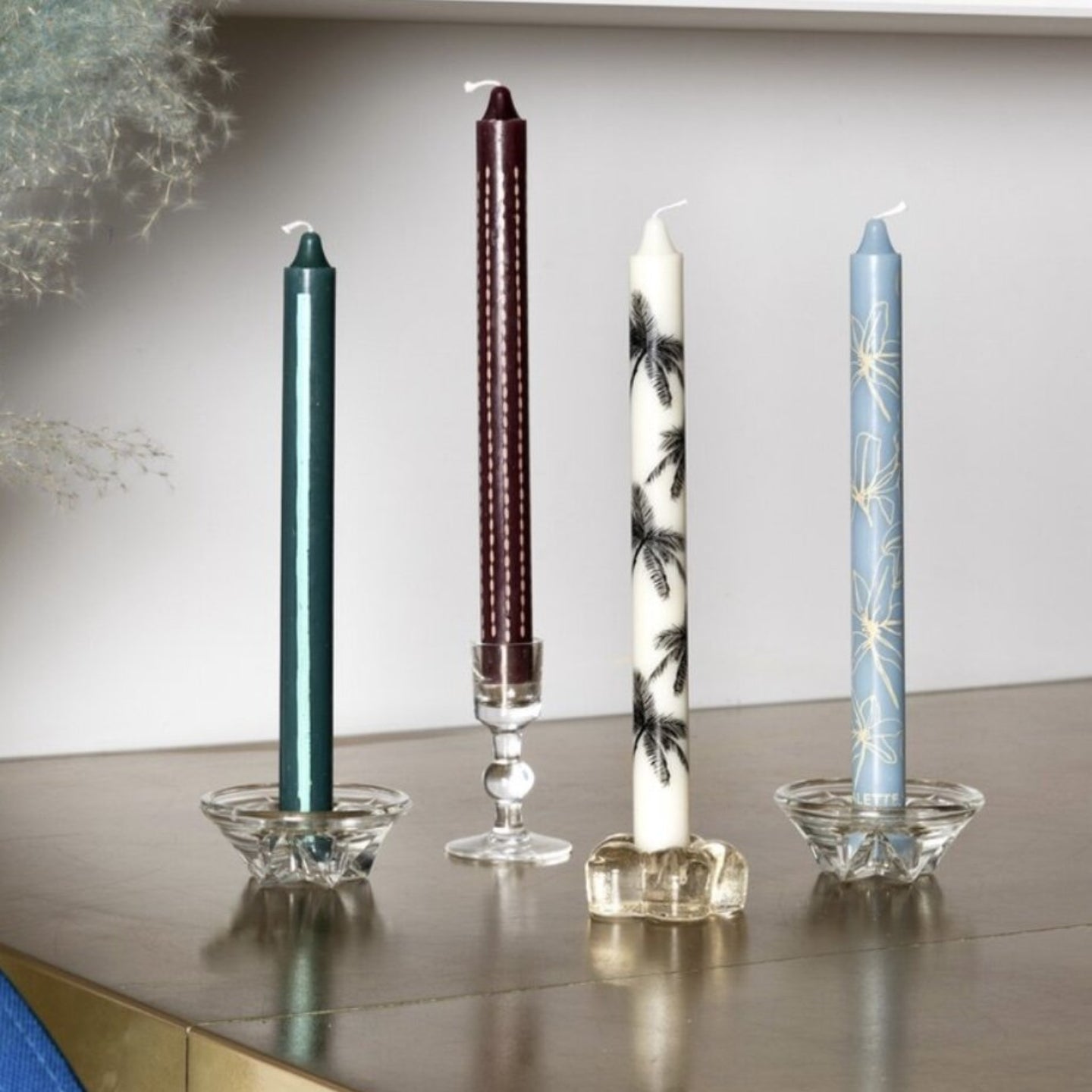 Four candles of different designs on a reflective surface with a neutral background