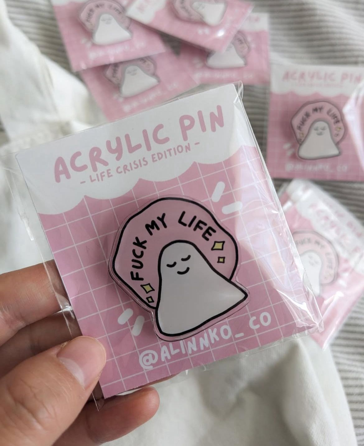 Acrylic pin with 'Fuck My Life' design in packaging held by a hand.