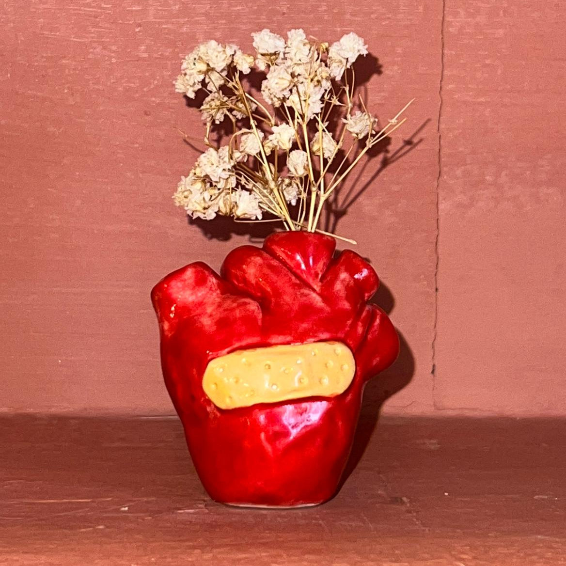 Red heart-shaped vase holding dried flowers against a red wall