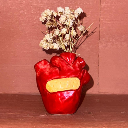 Red heart-shaped vase holding dried flowers against a red wall