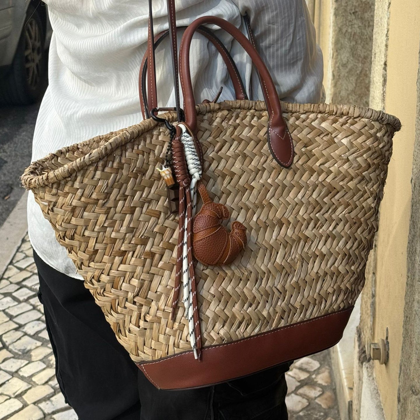 Person holding a woven bag with leather straps on a street.