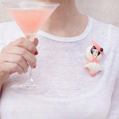 Person holding a cocktail with a shell-shaped brooch featuring a mermaid design.