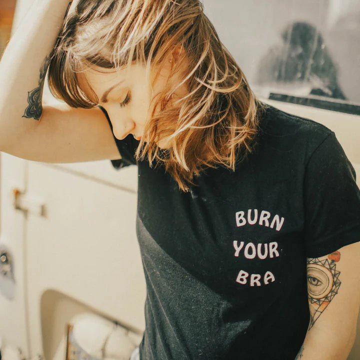 Person wearing a black t-shirt with 'Burn Your Bra' text in front of a vintage van.
