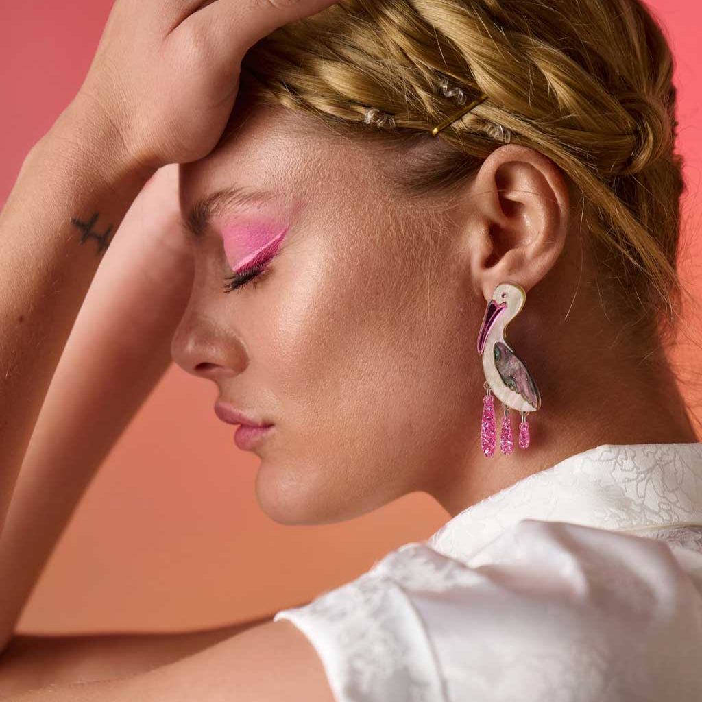 Woman with pink makeup and earrings against a pink background