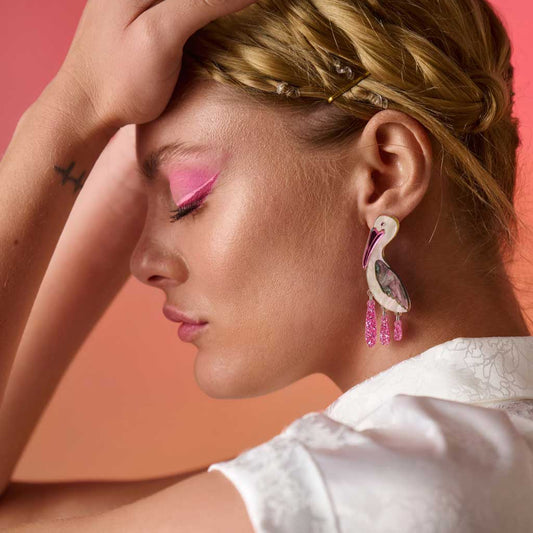 Woman with pink makeup and earrings against a pink background