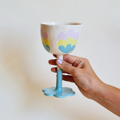 Hand holding a decorative ceramic cup with pastel floral design on a plain background