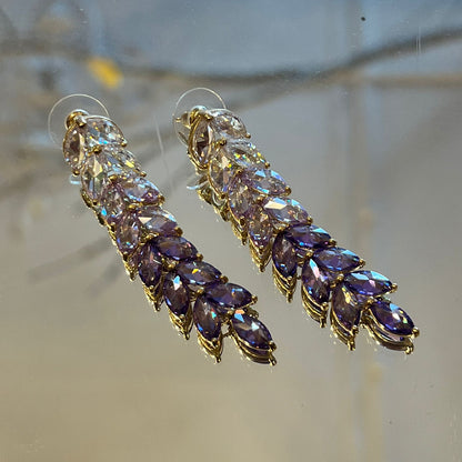 Pair of gold earrings with purple gemstones on a reflective surface