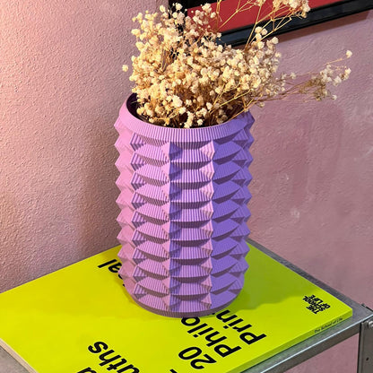 Purple textured vase with dried flowers on a green book against a pink wall