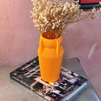 Yellow vase with dried flowers on a book against a pink wall
