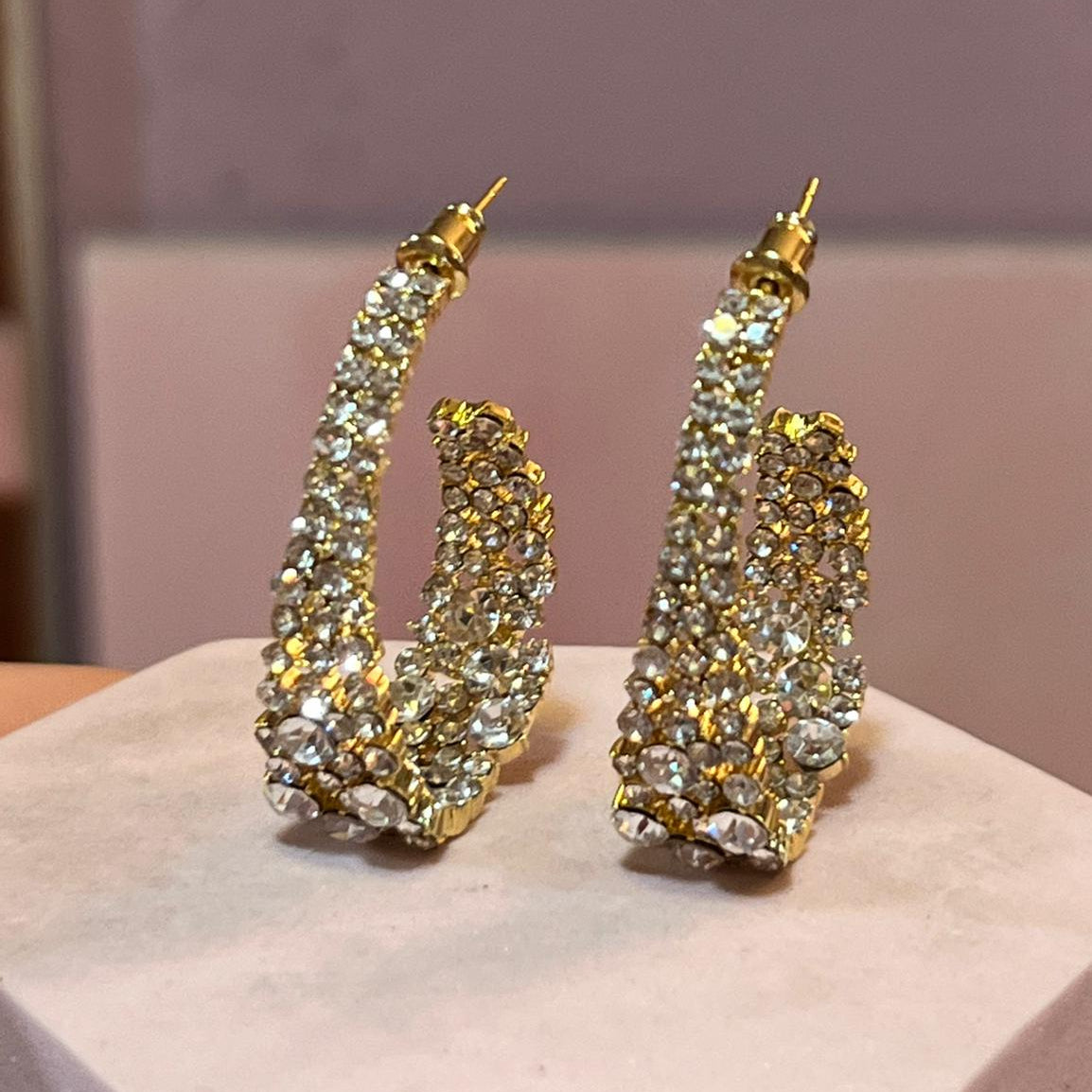 Gold and crystal earrings on a white stand with a blurred background