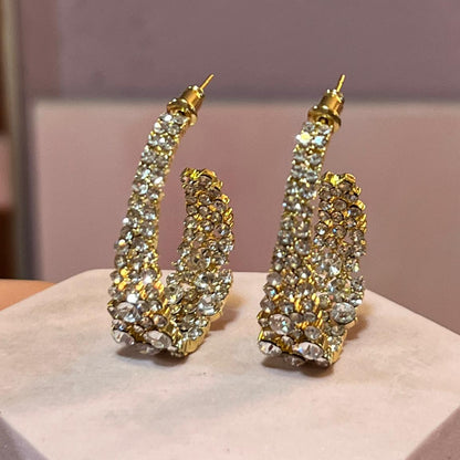 Gold and crystal earrings on a white stand with a blurred background