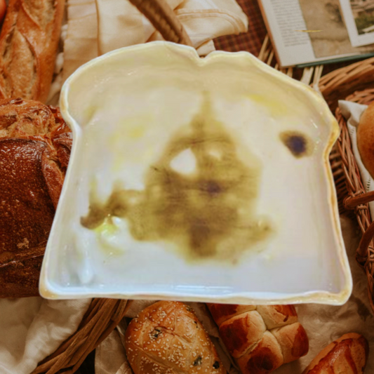 Artificial bread slice with brown spots on a woven surface with various bread loaves.