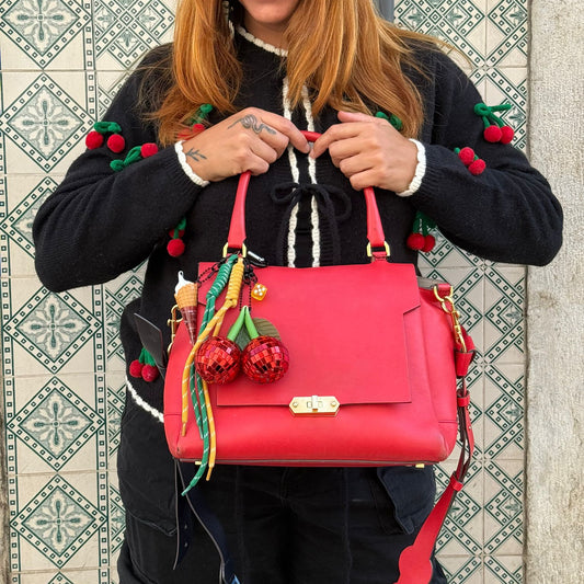 Woman holding a pink handbag with decorative elements against a patterned wall.