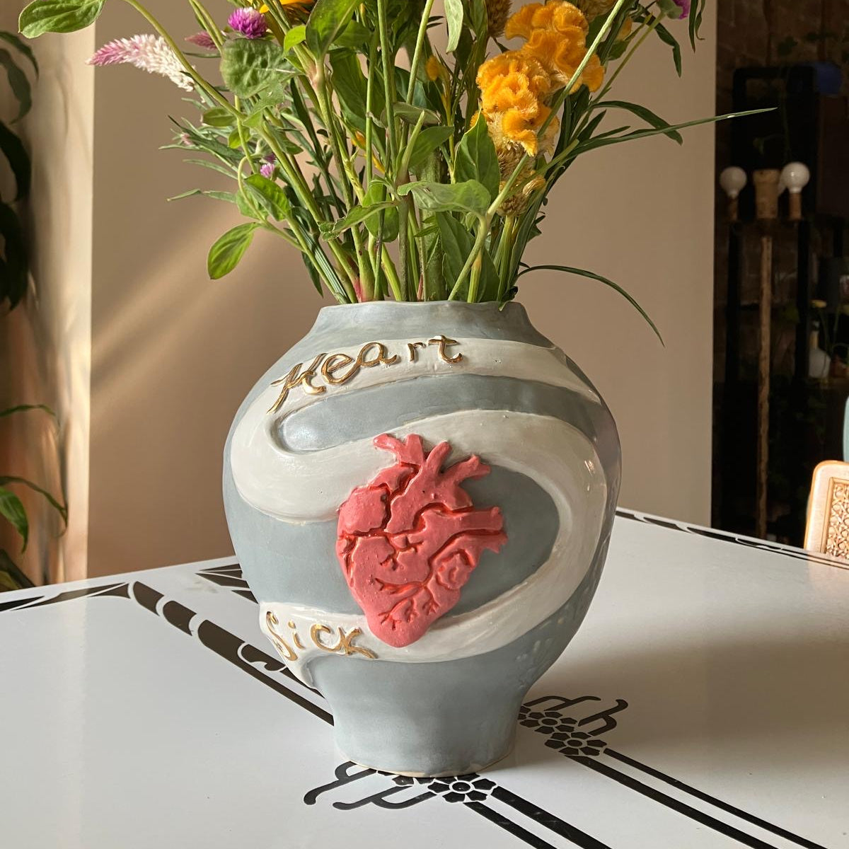 Decorative vase with a heart design on a table, filled with colorful flowers.