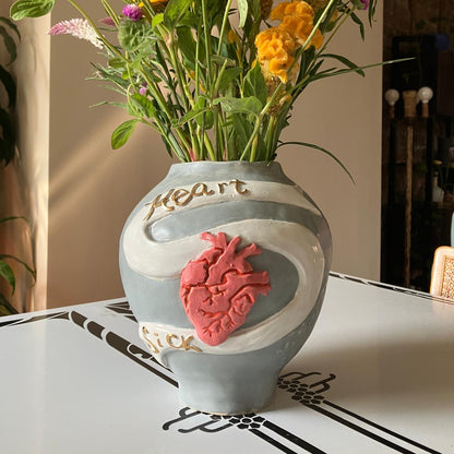 Decorative vase with a heart design on a table, filled with colorful flowers.
