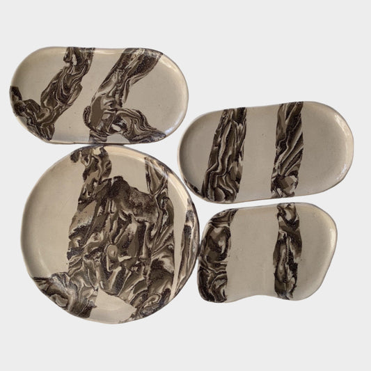 Set of four ceramic coasters with brown abstract patterns on a white fabric background